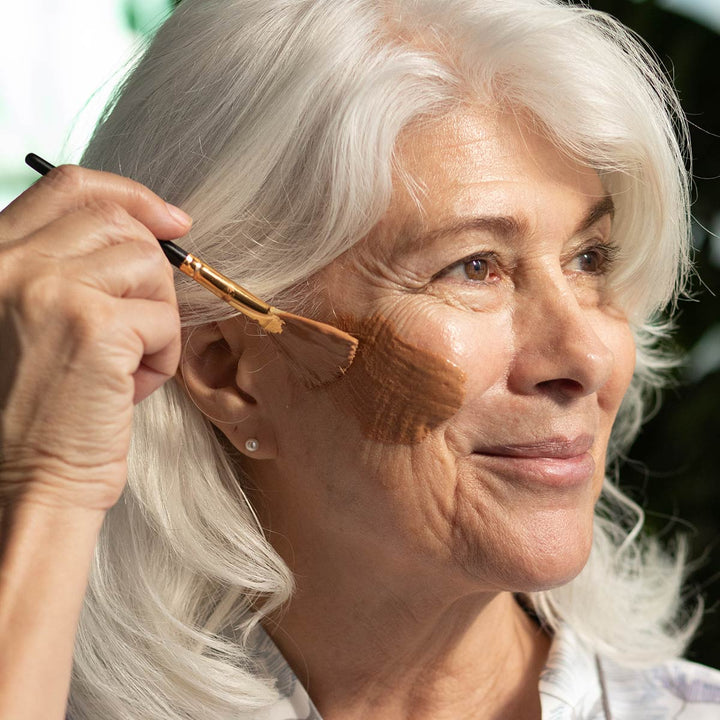 model applying french rose clay mask to face with natural boars hair brush