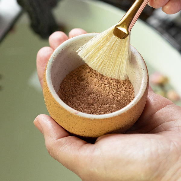french rose clay in ceramic mixing bowl in hand with natural boar hair bristle brush
