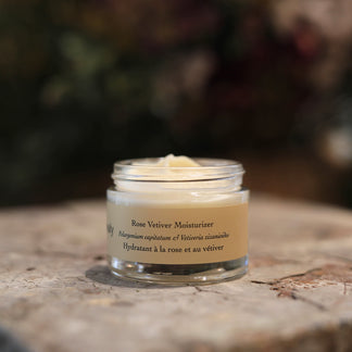 Front view of Rose Vetiver Moisturizer open jar showing cream texture on stone surface with blurred plant background