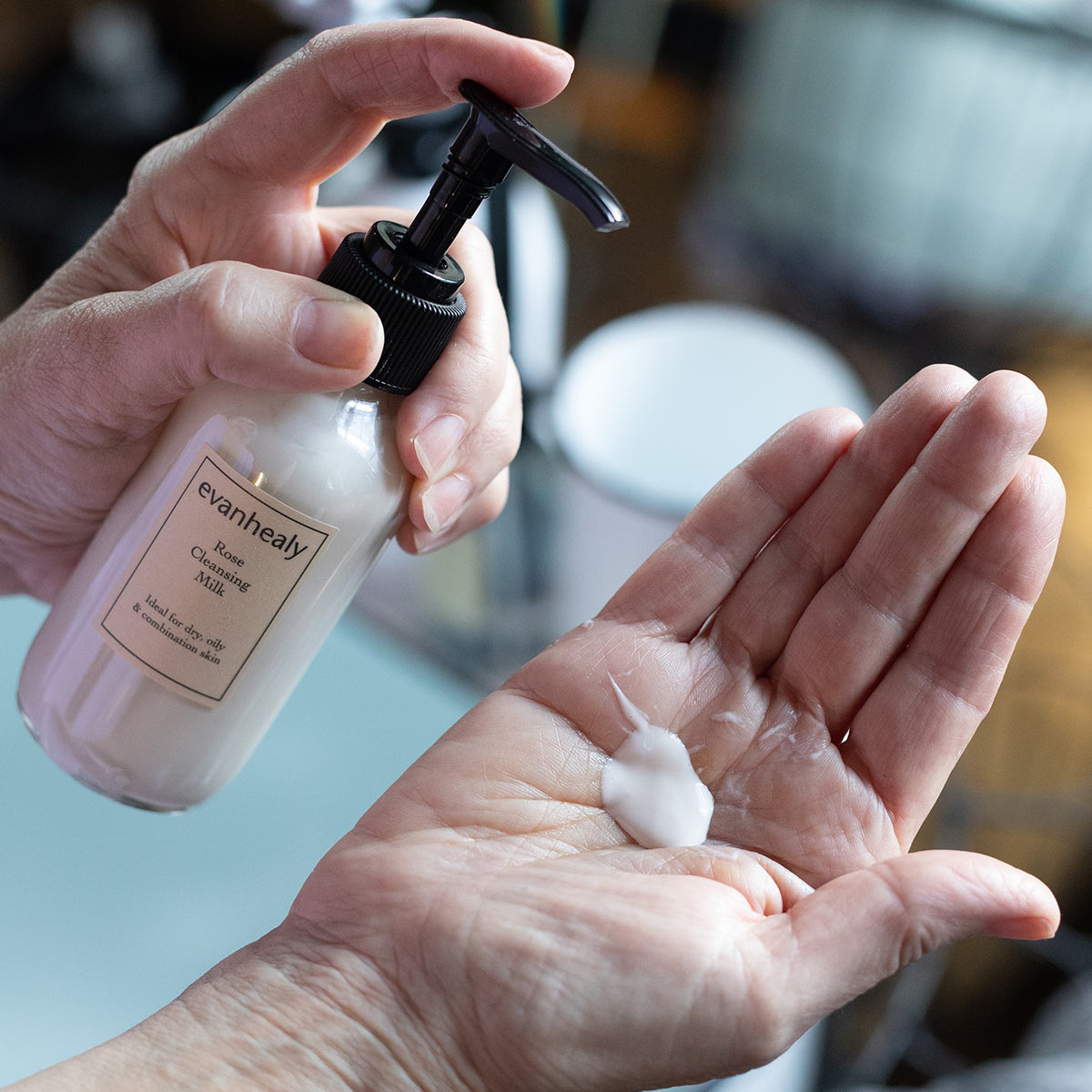 rose cleansing milk product with pump of cream cleanser in palm of hand