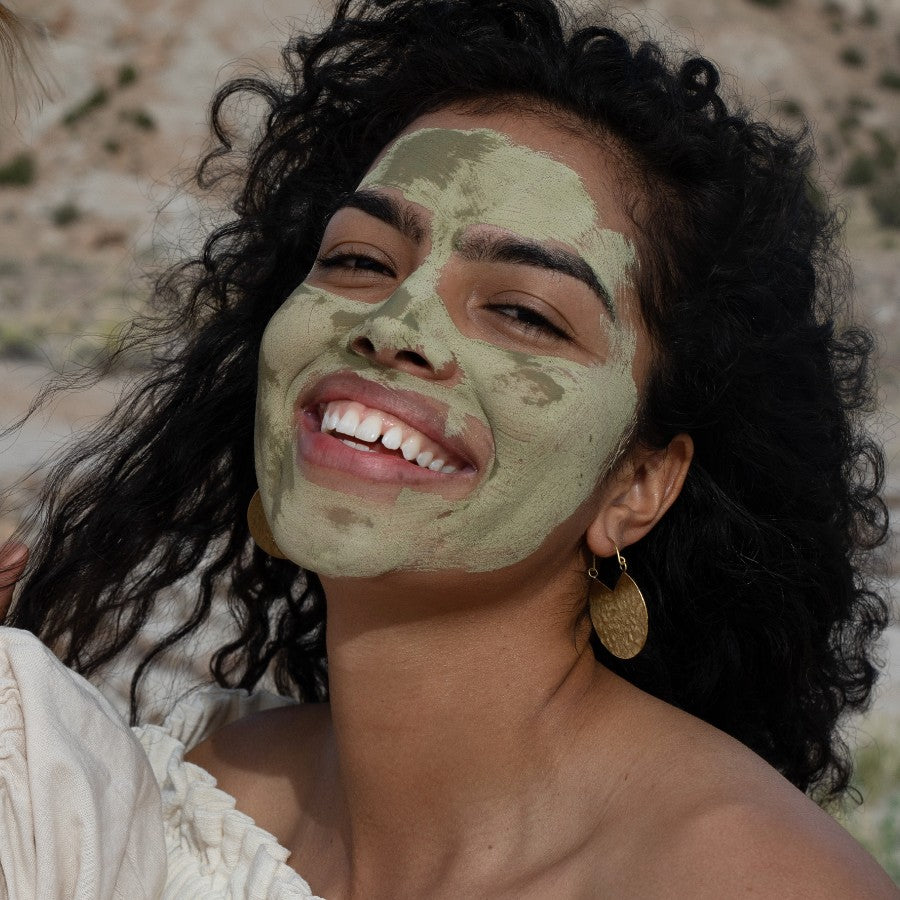 model smiling in santa fe desert with dry green tea clay mask natural facial exfoliator on face