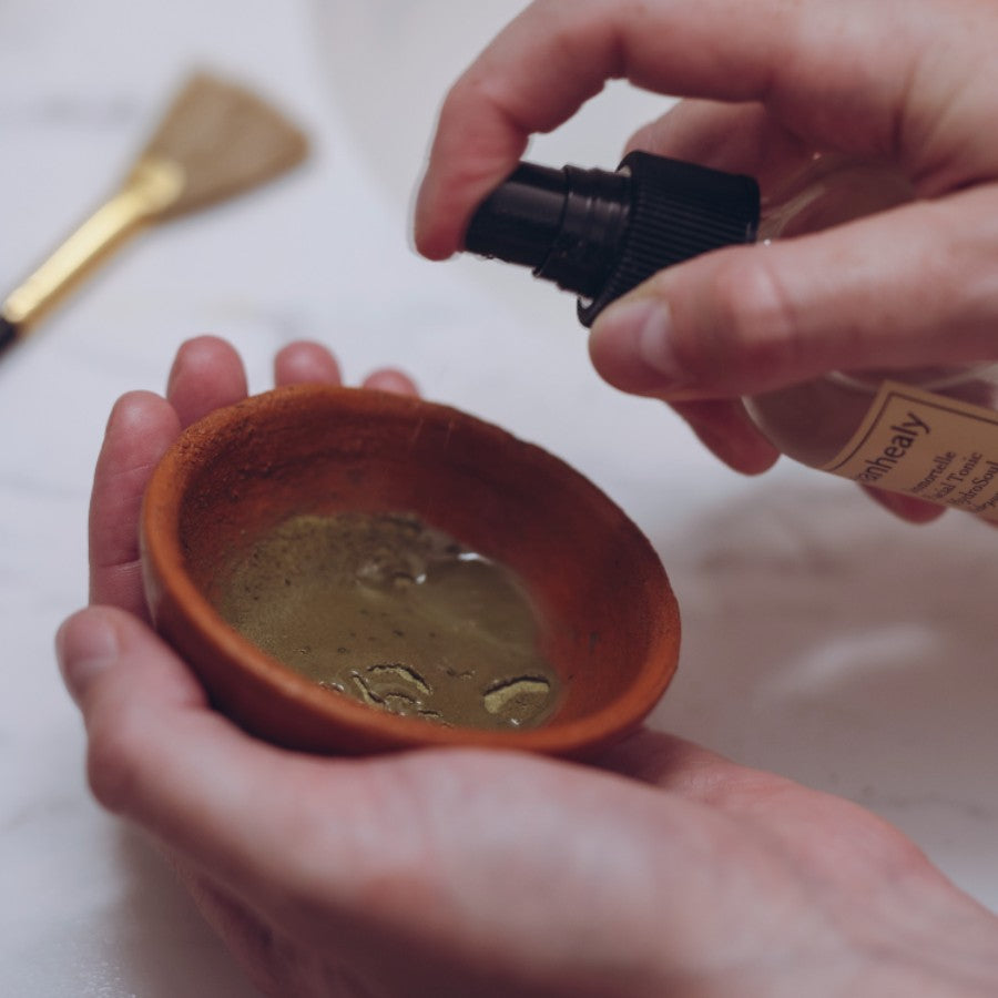 model spraying evanhealy hydrosol in terra cotta bowl with green tea clay