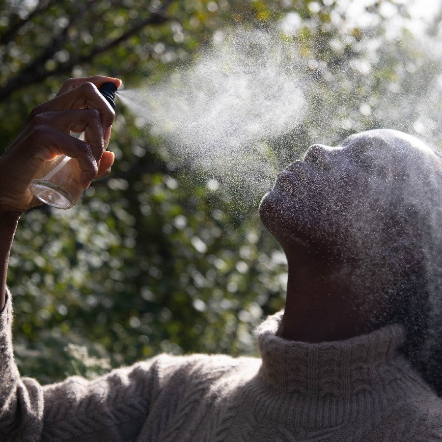 model spraying holy basil water tulsi hydrosol on face in nature