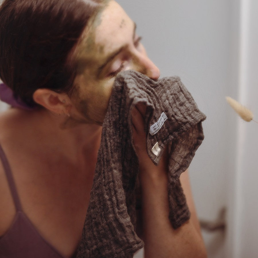 model wiping clay mask off face with linen face wash cloth in bathroom