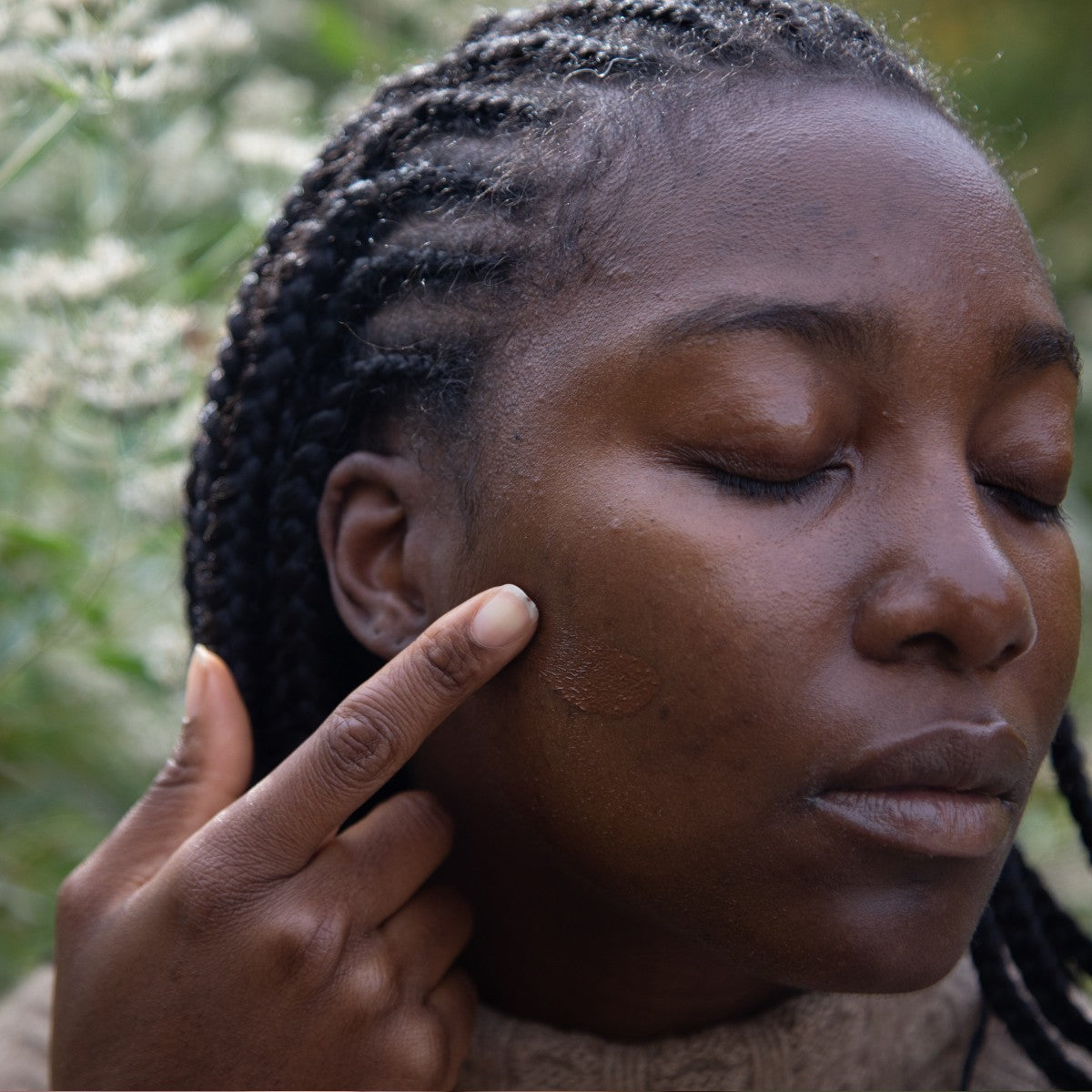 model applying tinted oil serum foundation on cheek with finger