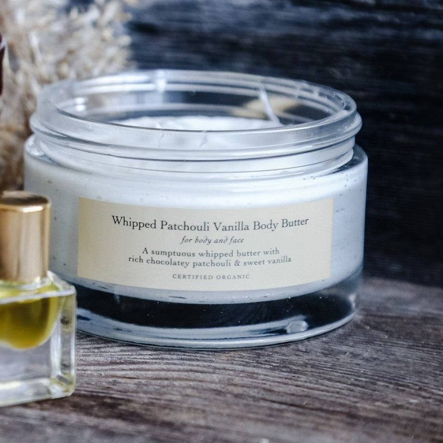 evanhealy whipped patchouli vanilla body butter on wooden surface next to perfume